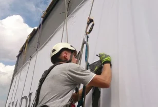 Wyklejanie szablonu logotypu na elewacji budynku przy wykorzystaniu technik alpinistycznych.