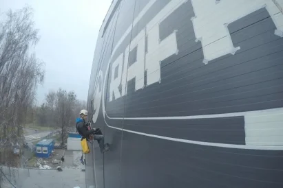 Malowanie loga na zewnętrznej ścianie hali produkcyjnej przy wykorzystaniu technik alpinistycznych.