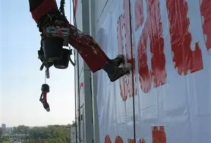 Wyklejanie szablonu loga na elewacji budynku przy wykorzystaniu technik alpinistycznych.