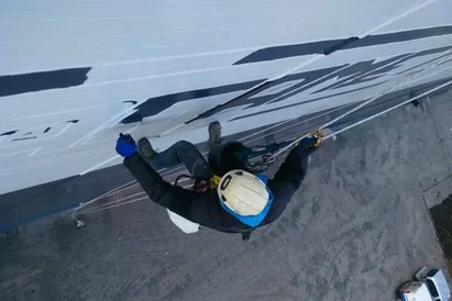 Malowanie loga na zewnętrznej ścianie hali produkcyjnej przy wykorzystaniu technik alpinistycznych.