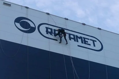 Malowanie loga na zewnętrznej elewacji hali produkcyjnej przy wykorzystaniu technik alpinistycznych.