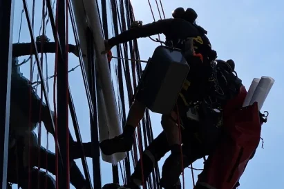 Dwóch alpinistów montuje folię na elewacji, tuż przy dużym logo firmy.