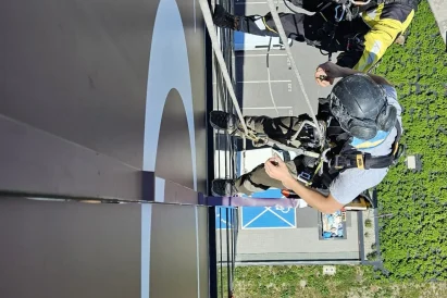 Dwóch alpinistów montuje folię na elewacji, tuż przy dużym logo firmy.